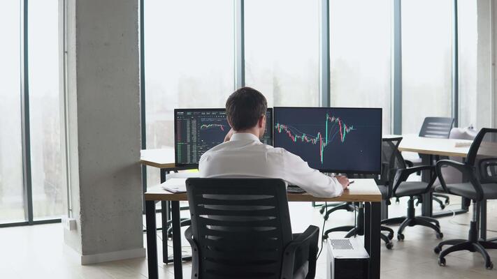 A man seated at a desk, working with multiple computer monitors displaying eFax alternatives.